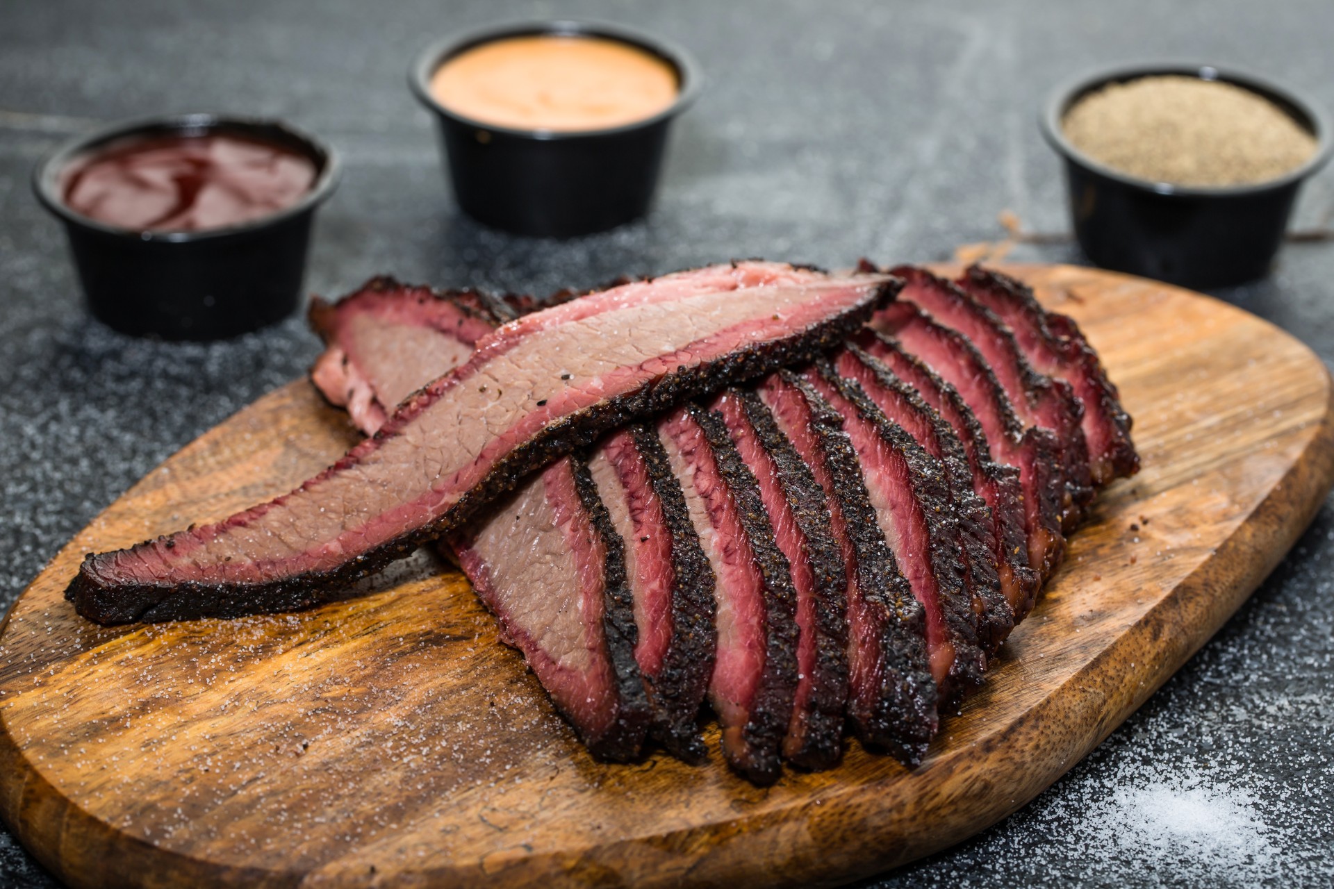 Beef Brisket platter steak meat sliced isolated on wooden board with dip sauce top view of grill food on dark grey background